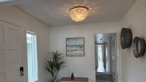 A hallway with a wooden floor, a white bench, a potted plant, a painting of a beach, and a ceiling light fixture. - Enjoy the beach life! Walk to beach and pier+Roof Deck& Garage in Hermosa Beach (Hermosa Beach)