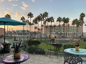 A terrace with outdoor seating, palm trees, and a view of a hotel building.