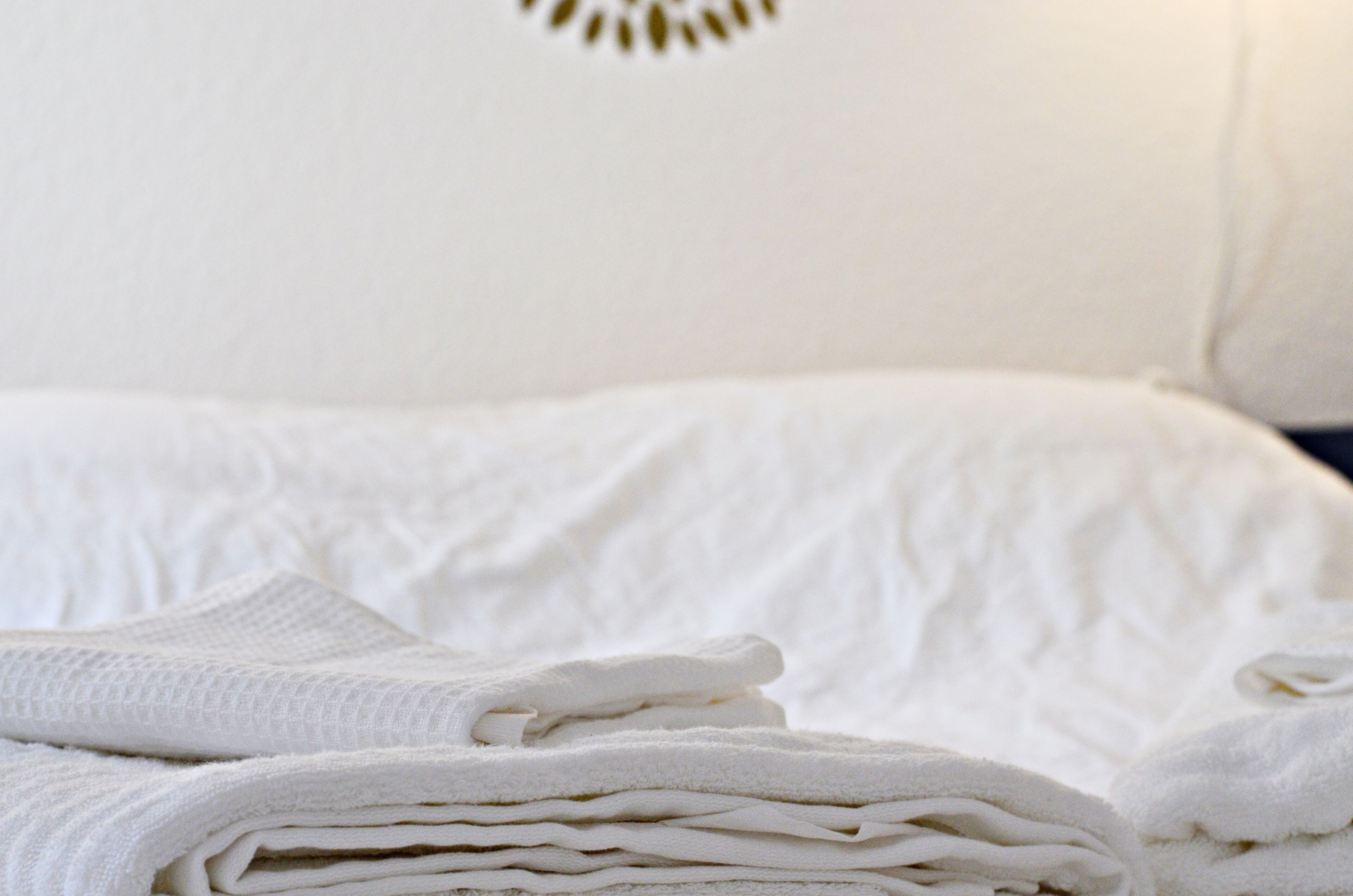 A neatly made bed with white linens and a folded towel on top.