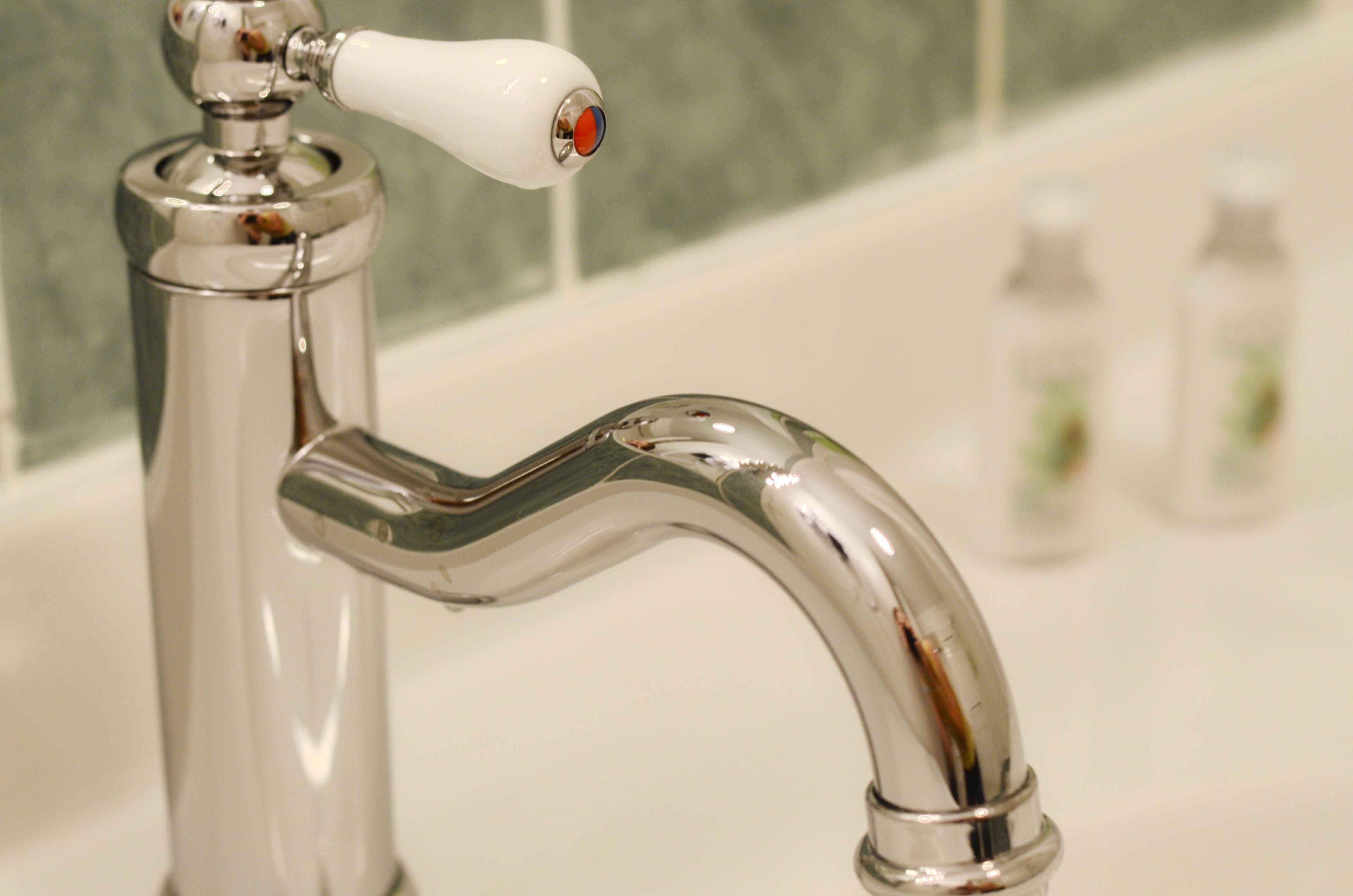 A chrome faucet with a white handle and a red button, set against a tiled wall.