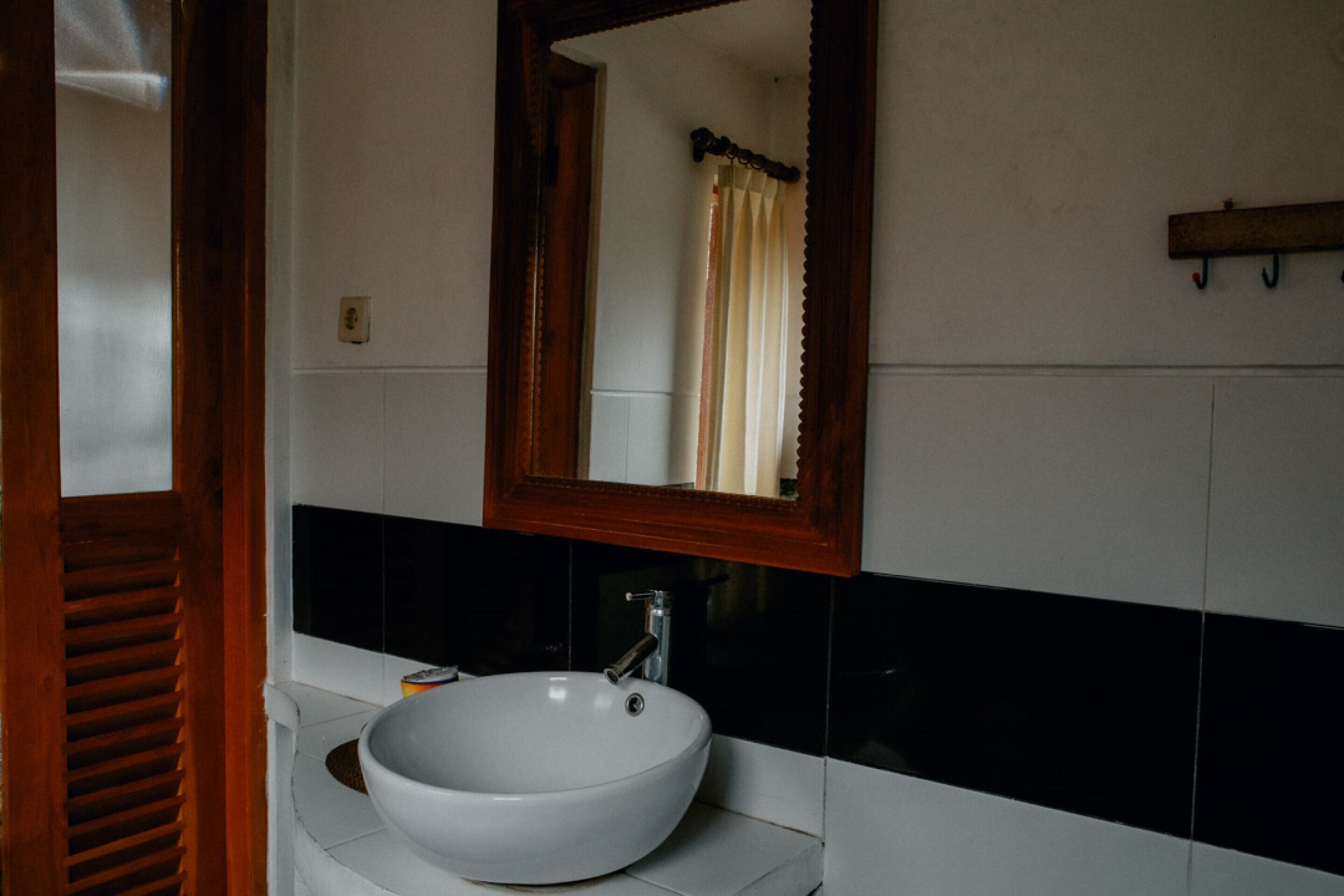 Un baño con un lavamanos blanco, un espejo con marco de madera y paredes con azulejos blancos y negros.