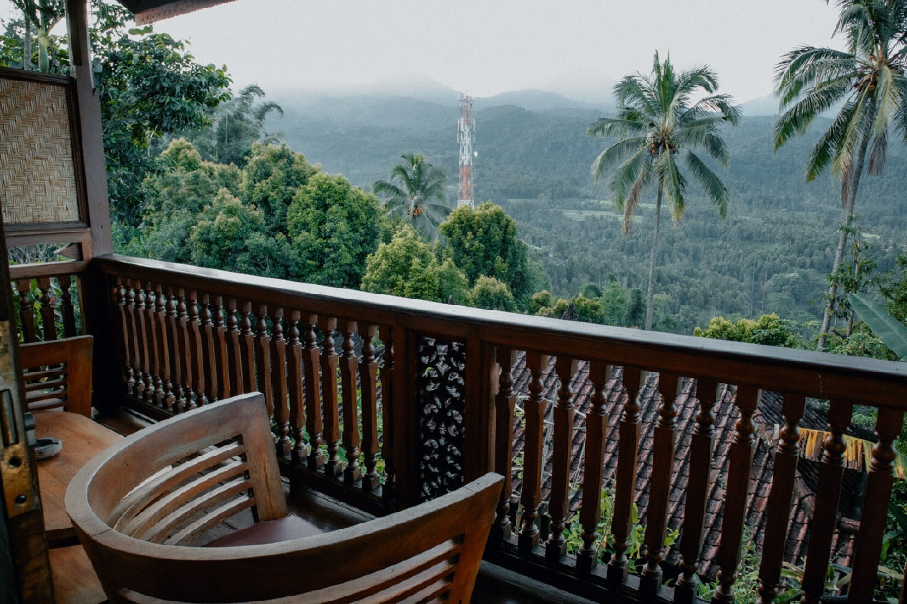 A wooden balcony with a view of a lush, green landscape and palm trees.