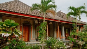 Un bâtiment traditionnel avec un toit en tuiles, des colonnes en bois et un jardin agrémenté de palmiers et de fleurs.