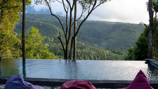 Une piscine à débordement offrant une vue sur une chaîne de montagnes boisées.
