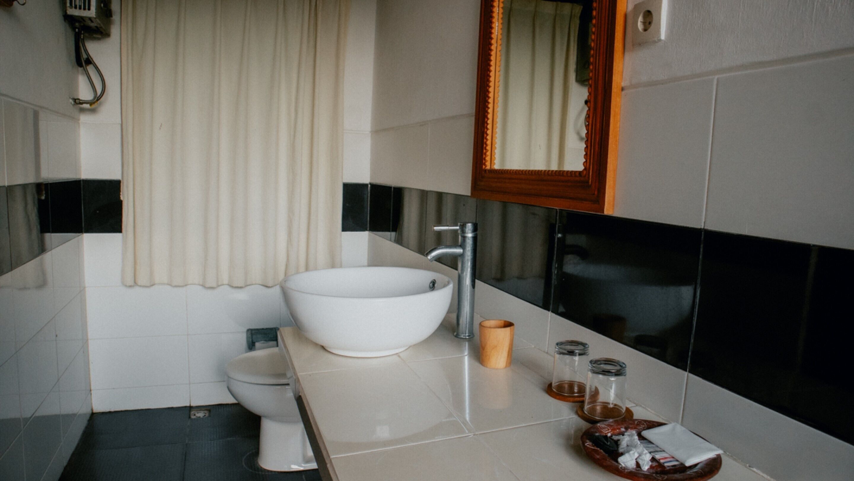 Un baño moderno con un lavamanos blanco de diseño, un inodoro, un espejo y una pequeña bandeja de madera con artículos de aseo.