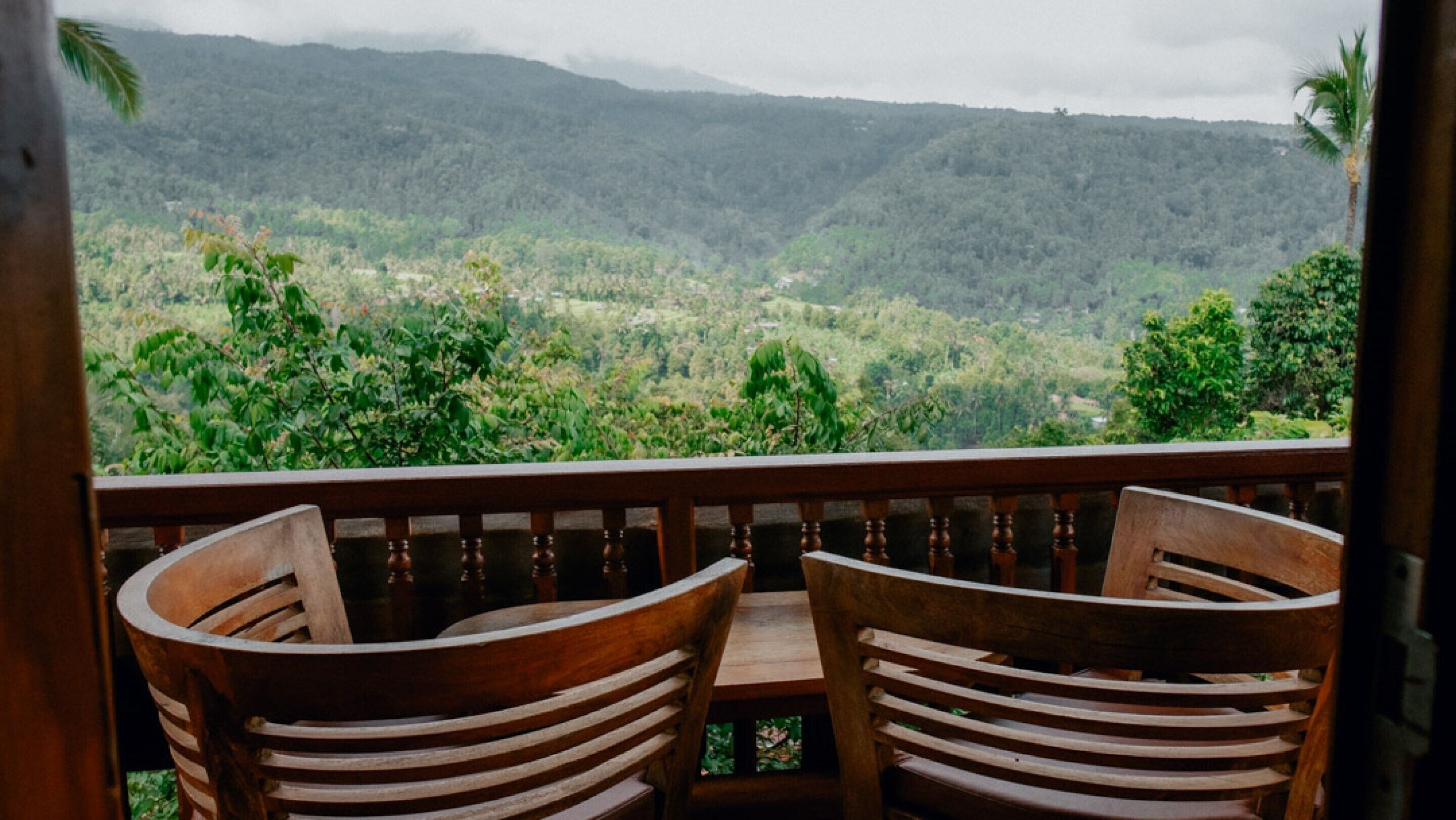 Une table et des chaises en bois sur un balcon offrant une vue sur une vallée verdoyante et des montagnes.