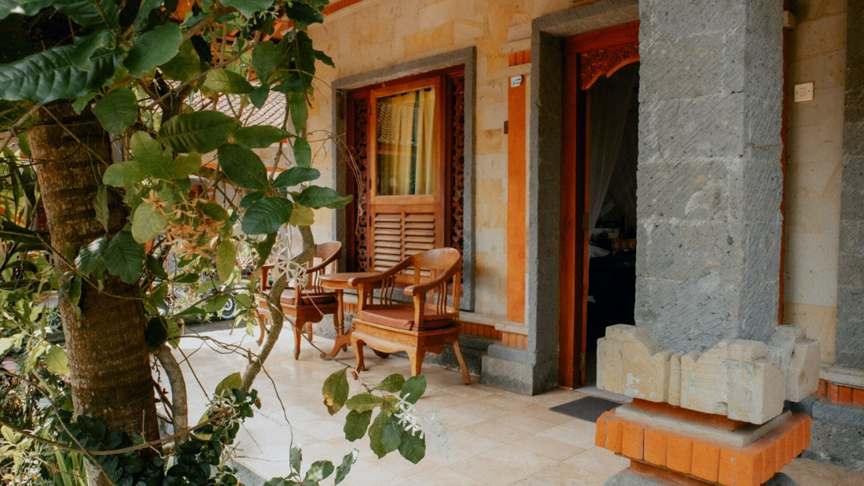 Un espace extérieur aménagé avec des meubles en bois, comprenant une table et des chaises, un pilier en pierre et une porte d’entrée donnant sur l’intérieur.