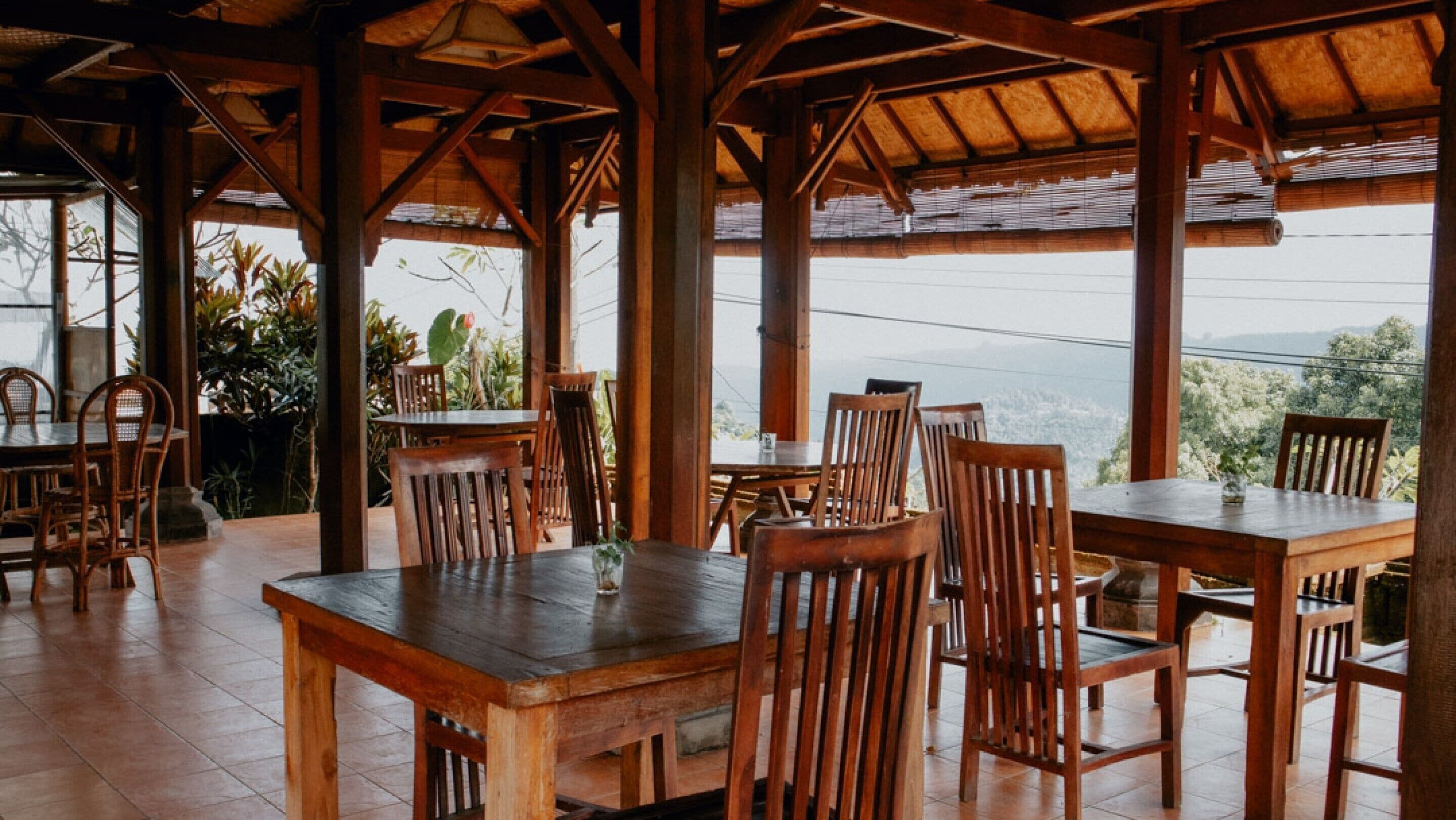 Un área de comedor al aire libre con mesas y sillas de madera, rodeada por una estructura de madera con techo de paja.