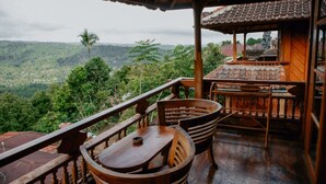 Une terrasse en bois avec une table et des chaises, offrant une vue sur une vallée verdoyante.