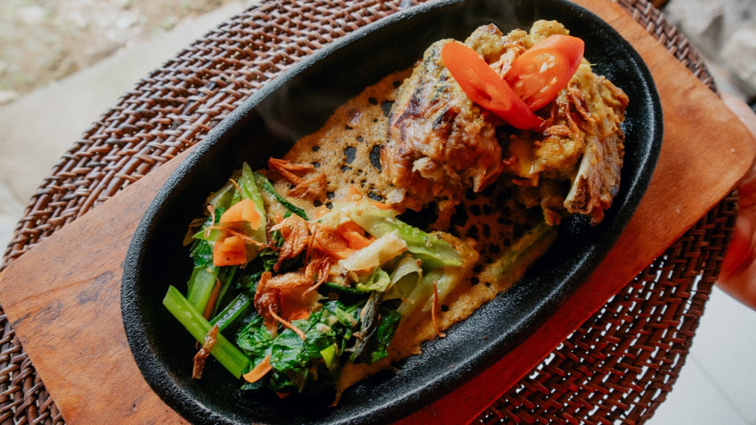 A dish with meat and vegetables on a black plate.