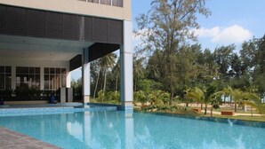 A swimming pool with a modern building in the background, surrounded by lush greenery. - Amerald Resort Hotel (Pengerang)