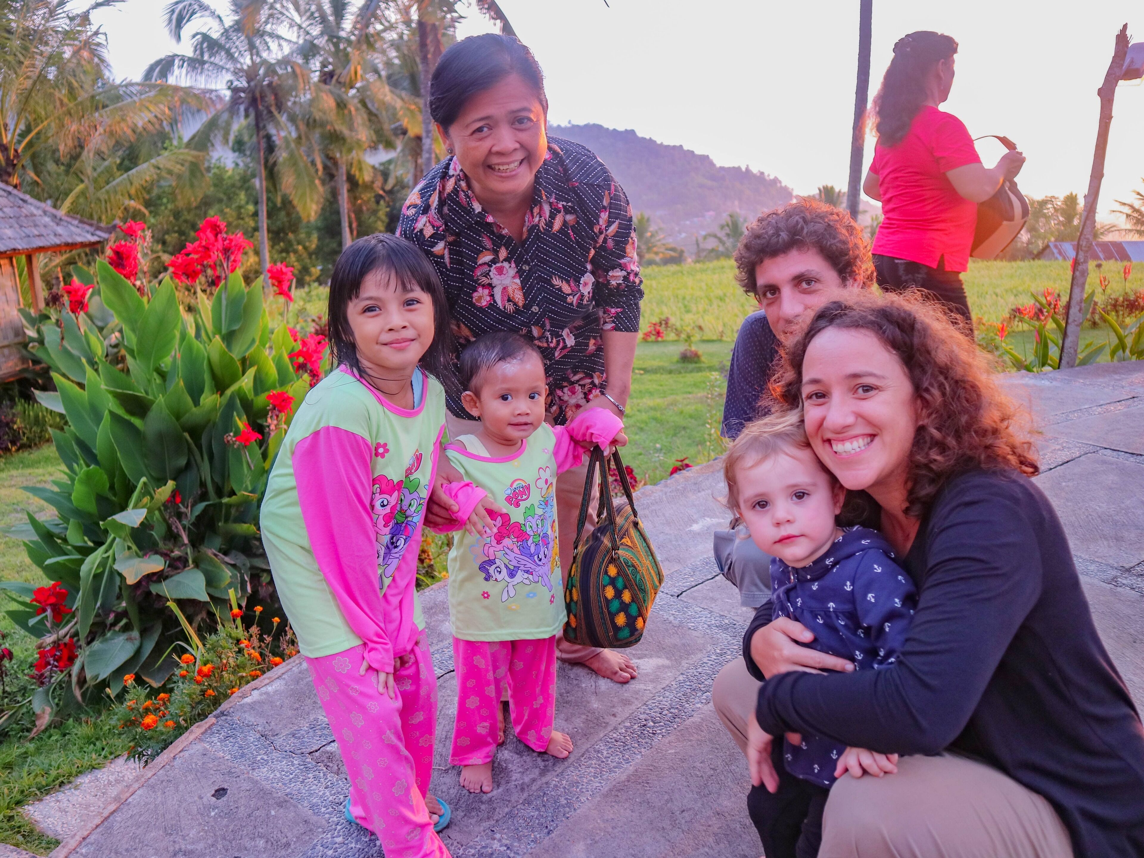 A group of people outdoors with a garden and palm trees in the background.