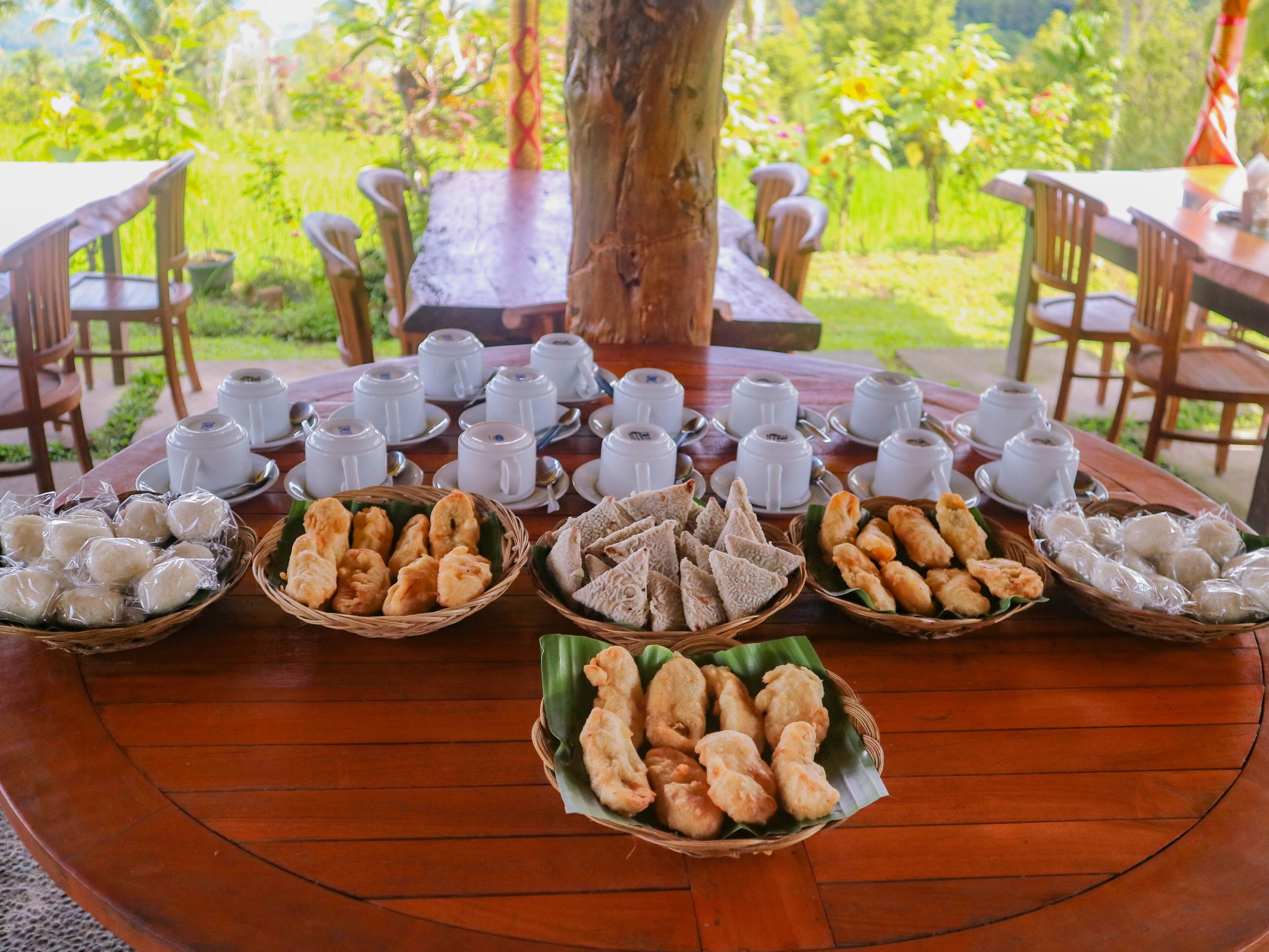 A round wooden table with white teacups and various food items in baskets.