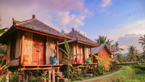 A row of traditional wooden houses with thatched roofs, surrounded by lush greenery and a clear sky. - Puri Sunny Camping (Munduk)