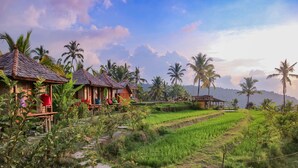 A rural landscape with thatched-roof huts, terraced rice fields, and palm trees. - Puri Sunny Camping (Munduk)