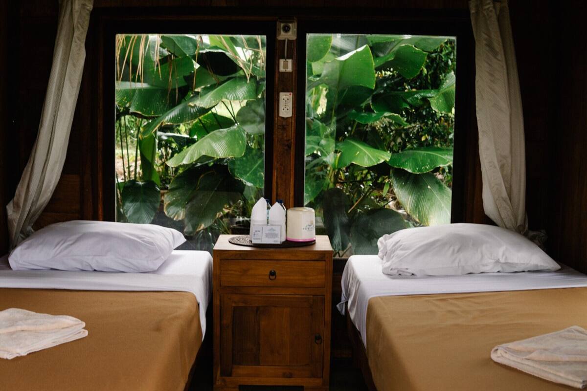 A room with two beds, a wooden nightstand, and a window with curtains.