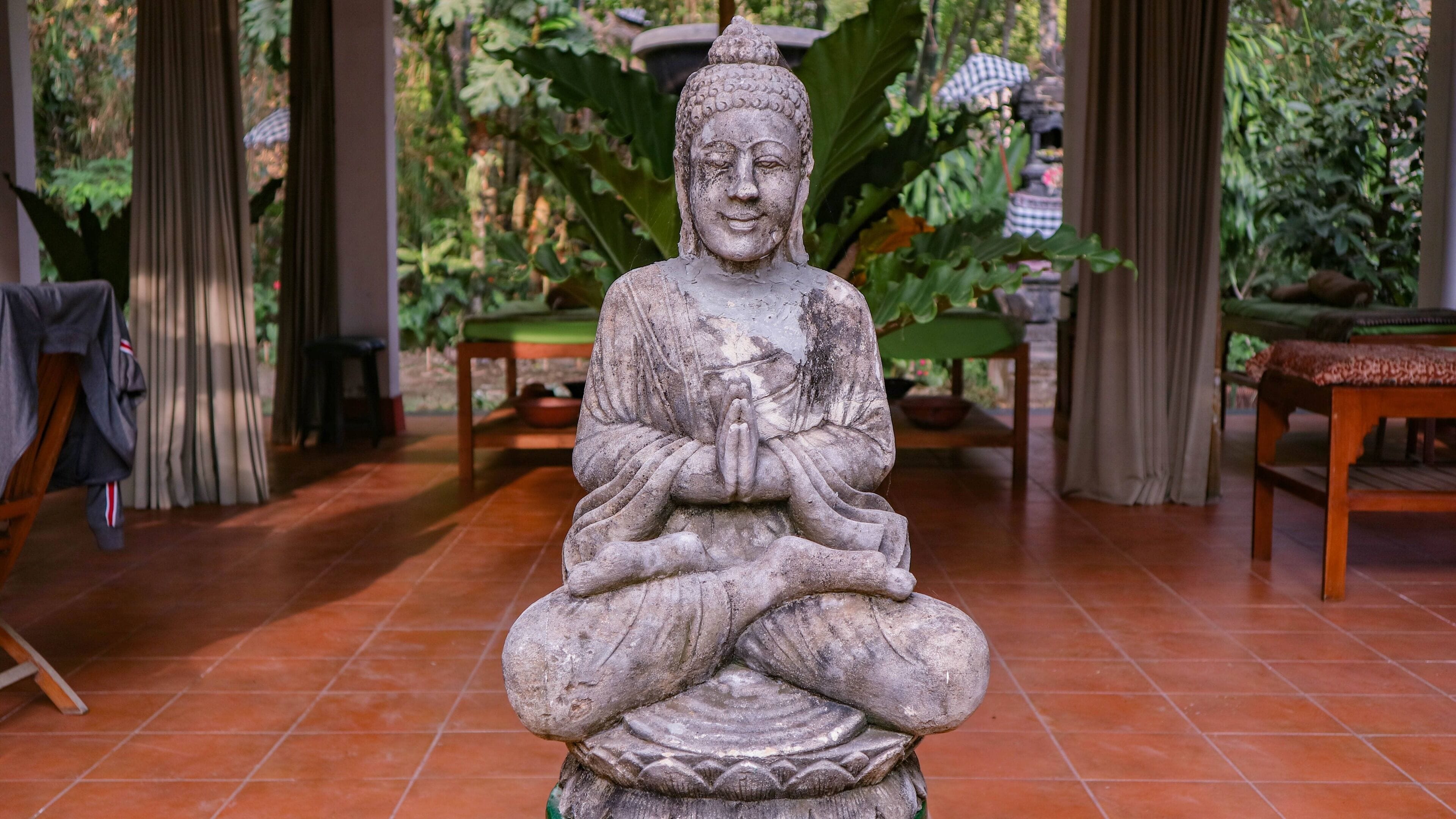 A stone statue of a seated figure in a room with tiled flooring, a green table, and a chair.