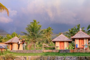 A tropical resort with wooden huts, palm trees, and a stone wall. - Puri Sunny Camping (Munduk)