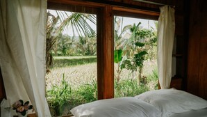 A bedroom with a large window, white curtains, and a bed with white linens. - Puri Sunny Camping (Munduk)