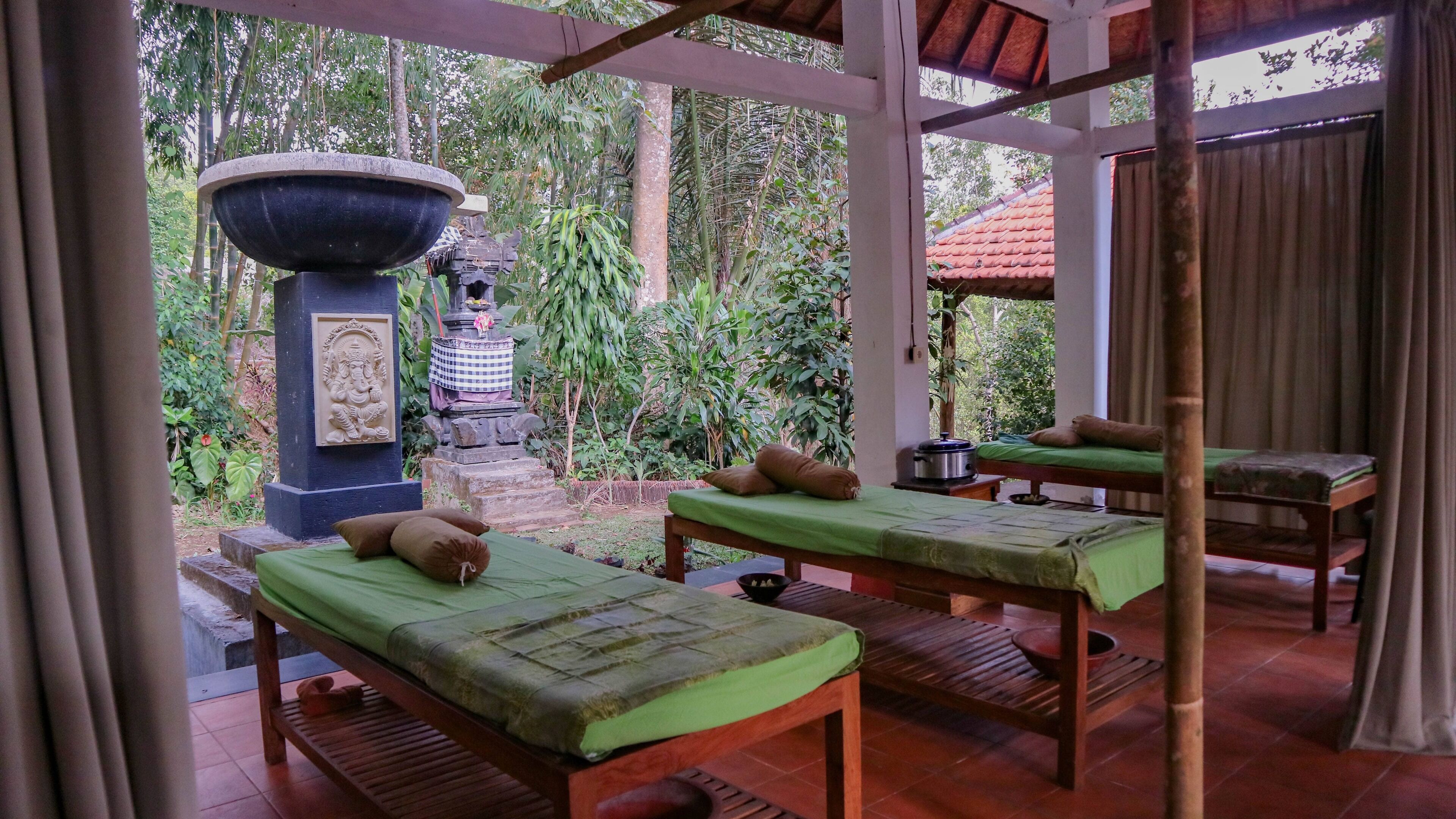 A traditional spa area with two massage tables, a stone basin, and a statue.