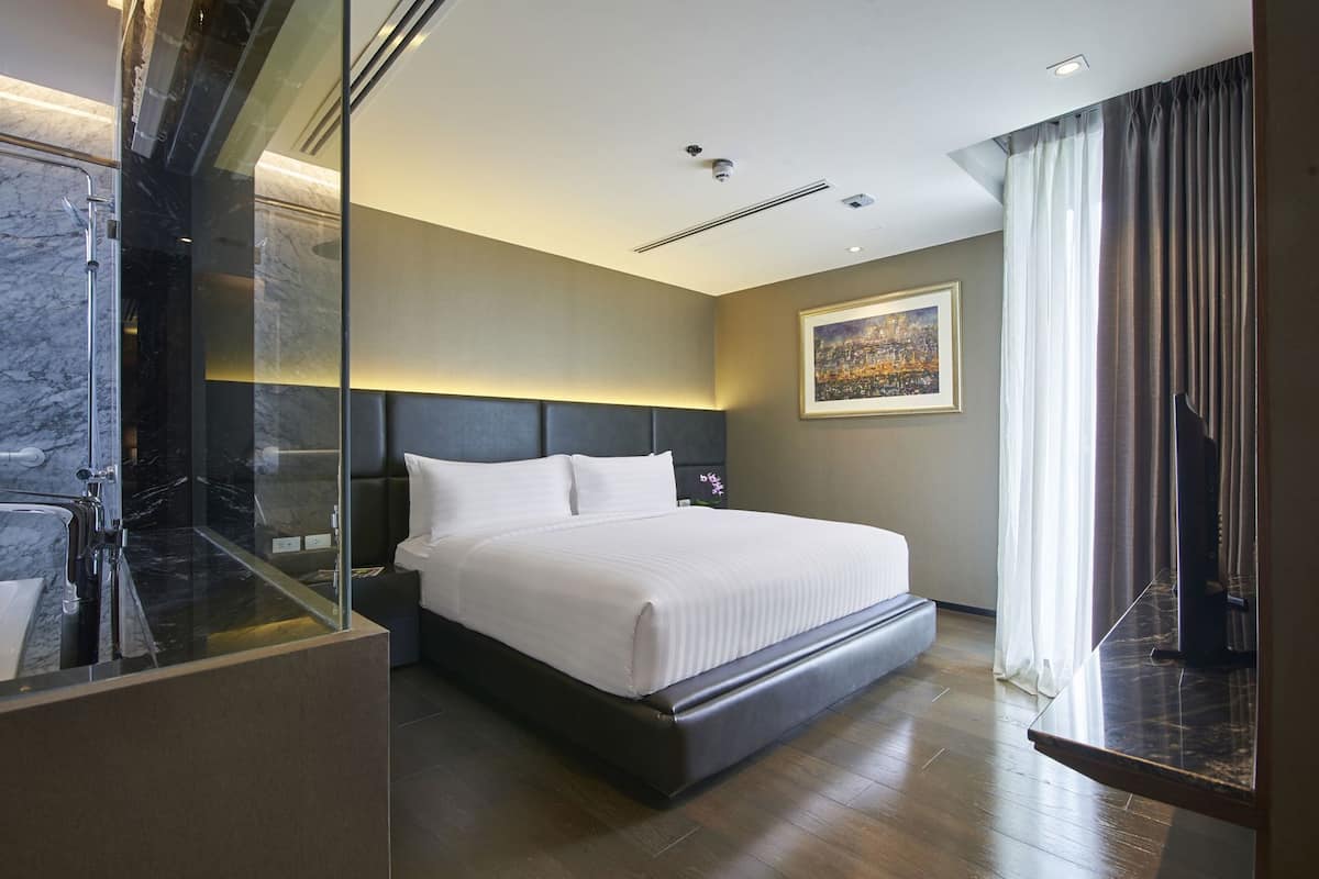 A modern hotel room with a large bed, a glass shower enclosure, and a cityscape painting on the wall.