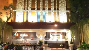Het exterieur van Sunrise Hotel Jombor met een moderne gevel, verlichte signage en een zichtbaar café genaamd 'ORTUS Cafe' bij de ingang.