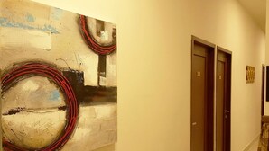 Een gang met een groot abstract schilderij links, twee deuren met nummers, en een kamerbreed gordijn rechts.