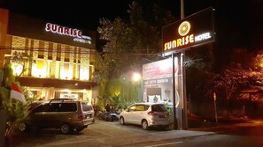 A hotel named Sunrise Hotel with a prominent sign, parked cars, and a well-lit entrance.