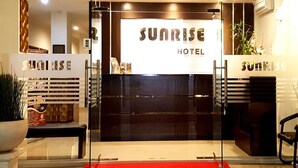 De ingang van Sunrise Hotel met een rode loper, glazen deuren en een bord boven de entree.