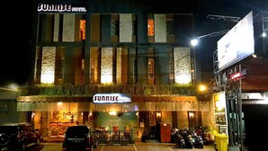 Un hotel con un letrero que dice "Sunrise Hotel" y una entrada visible con un área de estacionamiento.