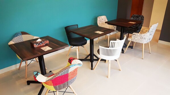 A dining area with a teal wall, wooden tables, and chairs with various patterns. - Sunrise Hotel Jogja (Depok)