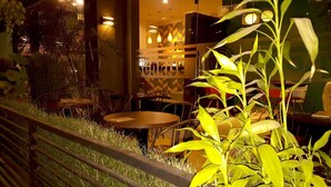 Un comedor interior con mesas y sillas, rodeado de follaje e iluminación decorativa.