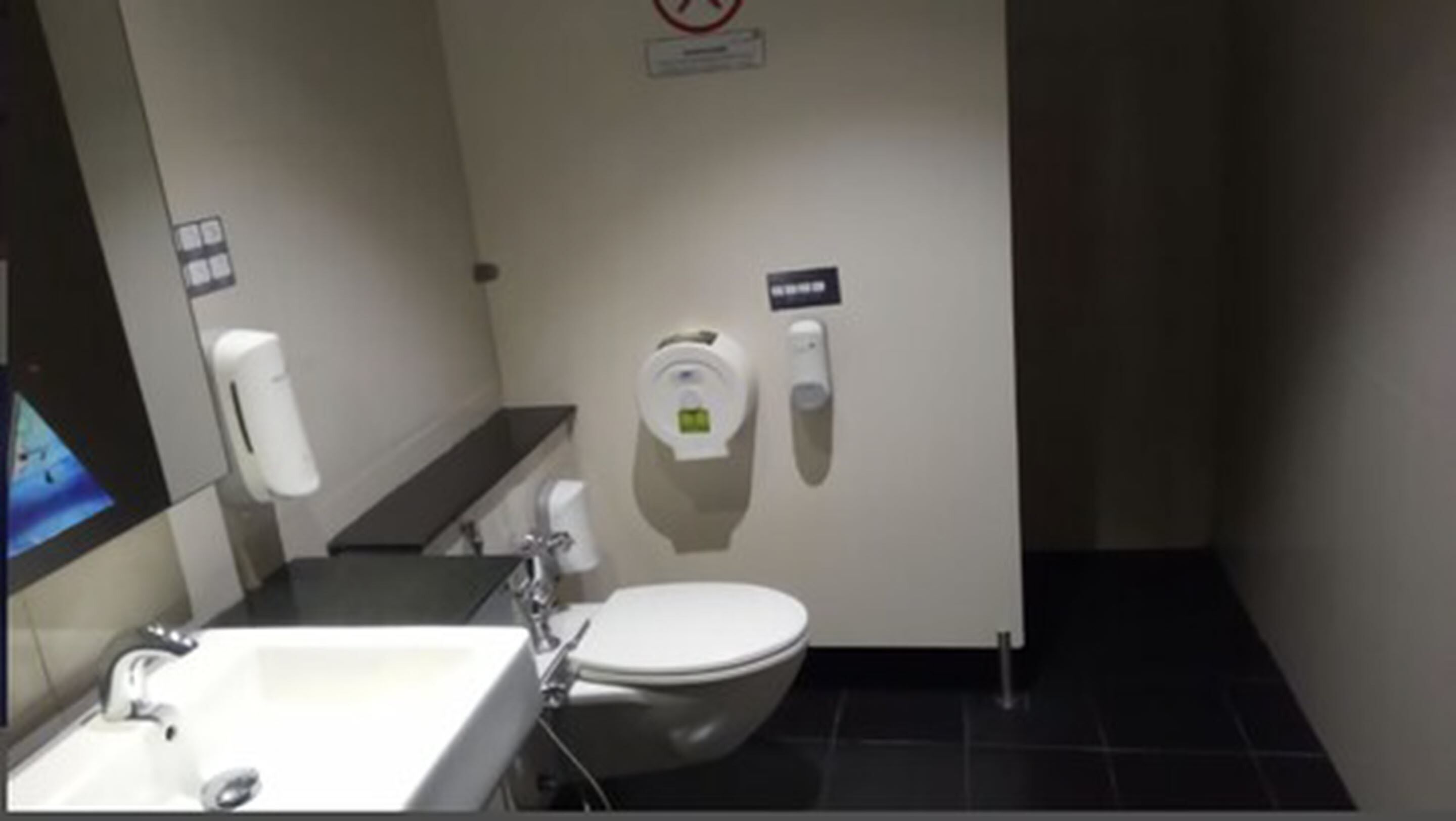 Um banheiro com vaso sanitário, secador de mãos e dispensador de sabonete na parede.