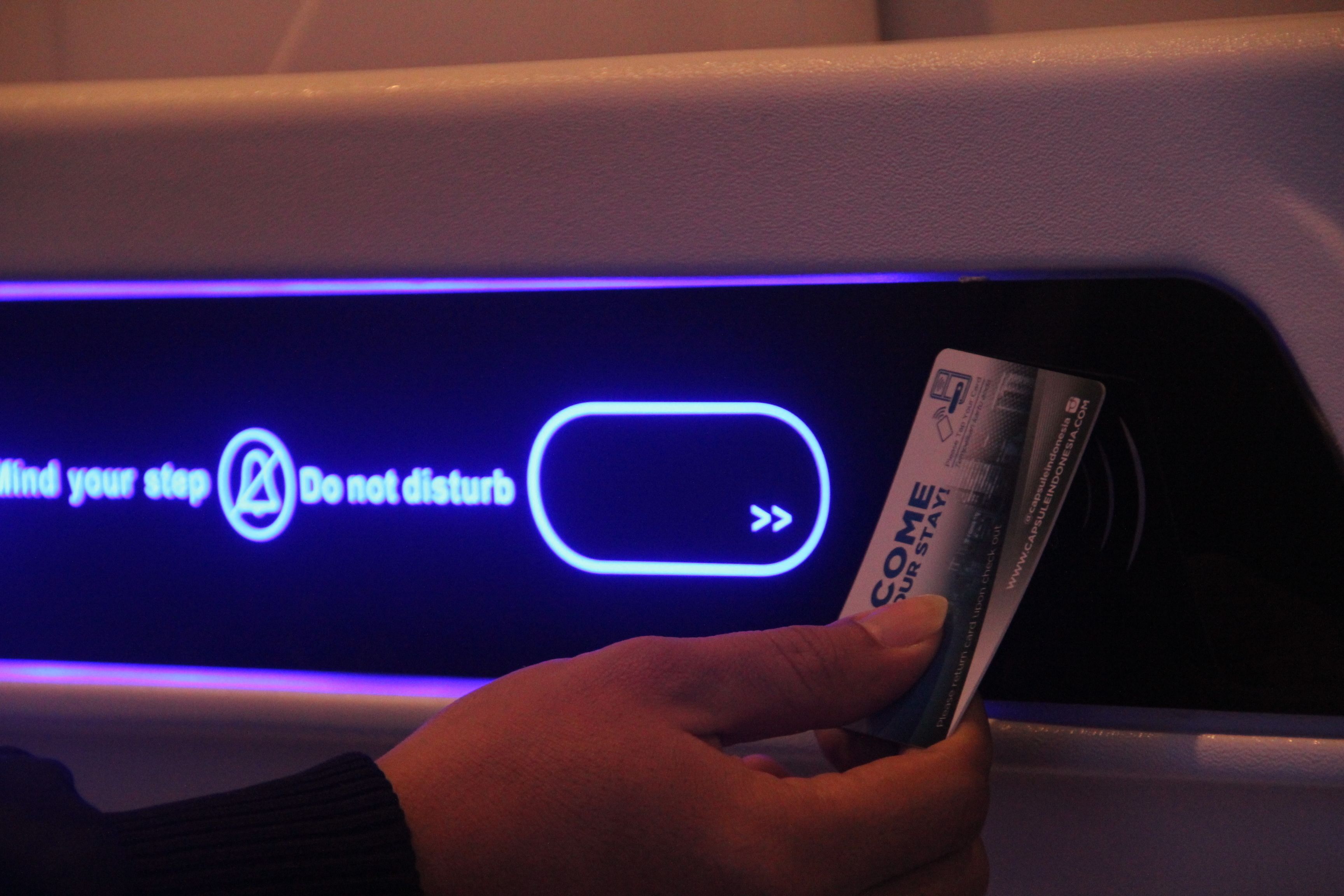 A hand holding a card near a digital display with a message and a symbol indicating a step or action.