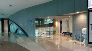 A modern hotel lobby with a glass facade, a visible escalator, and a sign for the 'POMTANE HOTEL'. - PassGo Digital Airport Hotel Terminal 3 Soekarno Hatta (Tangerang)