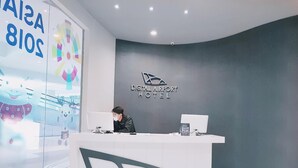 A reception desk at the Digital Airport Hotel with a modern design, a logo on the wall, and a glass wall with a colorful display. - PassGo Digital Airport Hotel Terminal 3 Soekarno Hatta (Tangerang)