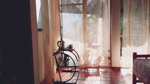 A room with a wooden floor, a metal-framed chair, a bed, and a window with sheer curtains. - Ella camping Resort (Ella)