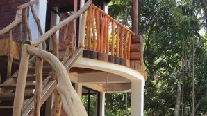 A wooden staircase with a railing, leading to a covered area with a view of surrounding trees. - Ella camping Resort (Ella)