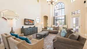 Un salon spacieux doté d’une grande fenêtre, d’une cheminée et d’un lustre moderne.