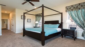 A four-poster bed in a bedroom with a ceiling fan, a nightstand, and a window with curtains.
