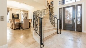 Un hall d’entrée spacieux avec un escalier en marbre, une salle à manger agrémentée d’un lustre et une grande porte ornée de panneaux de verre décoratifs.