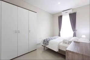 Un dormitorio con cama, armario y ventana con cortinas.