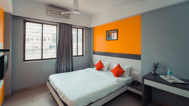 A modern hotel room with a bed, a desk, a chair, a telephone, and a window with curtains. - Hotel Aashish Deluxe Kolhapur (Kolhapur)