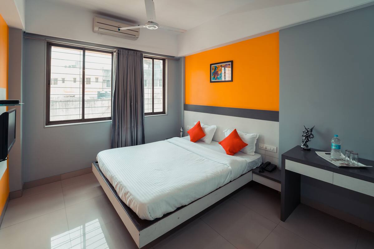 A modern hotel room with a bed, a desk, a chair, a telephone, and a window with curtains.