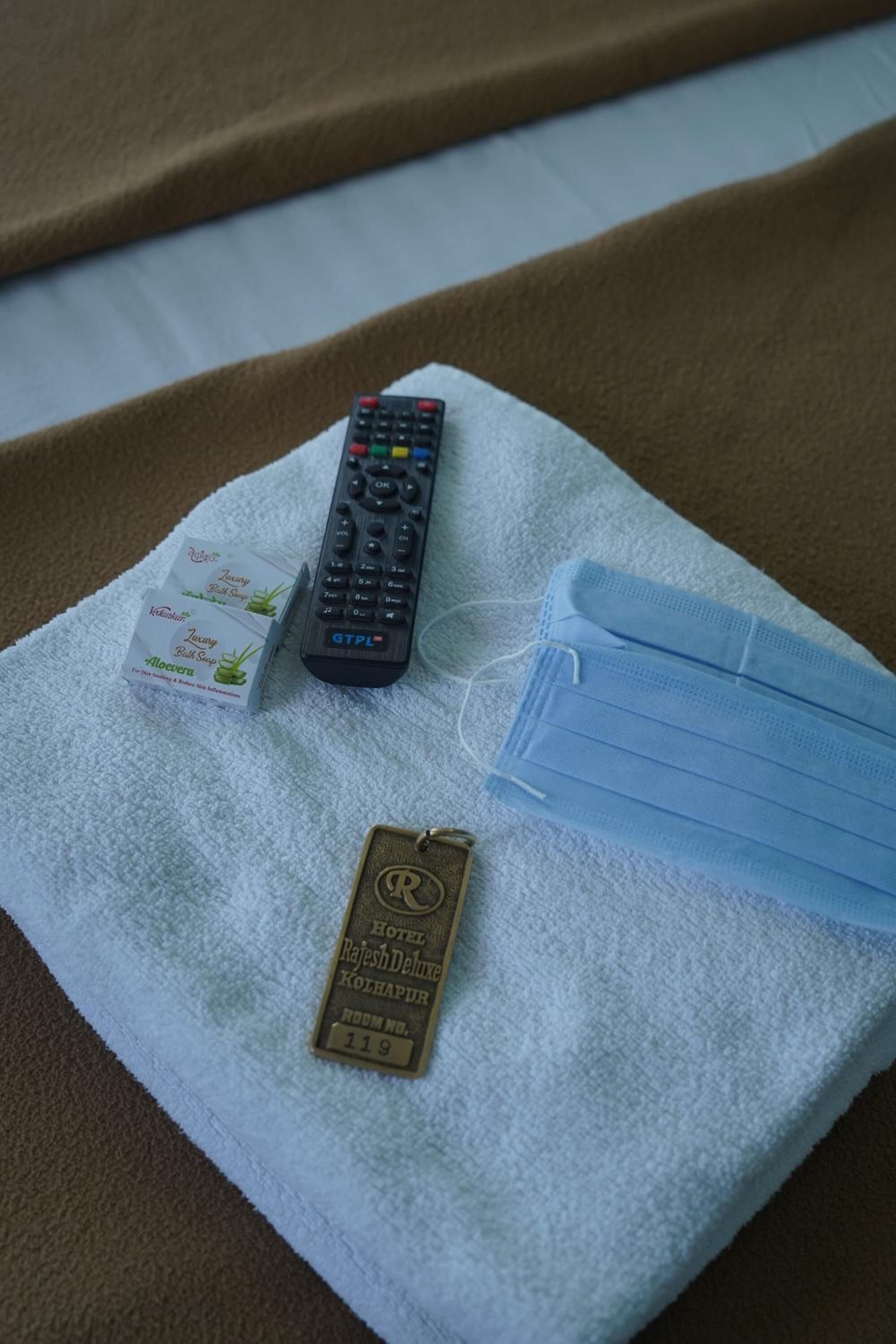 A remote control, a face mask, and a hotel keychain on a towel.