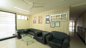 A waiting area with leather sofas, a glass coffee table, ceiling fans, and framed certificates on the wall. - Hotel Aashish Deluxe Kolhapur (Kolhapur)