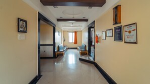 A hotel corridor with a modern design, featuring a wooden ceiling, framed pictures, and a seating area with two sofas and a table. - Hotel Aashish Deluxe Kolhapur (Kolhapur)