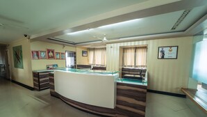 A reception area with a curved reception desk, a ceiling fan, and framed pictures on the walls. - Hotel Aashish Deluxe Kolhapur (Kolhapur)