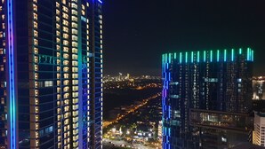 A high-rise building with illuminated windows and a view of a cityscape at night. - Cosmy Orchard Apartment (Surabaya)