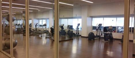 A gym with exercise equipment, large windows, and a polished wooden floor.